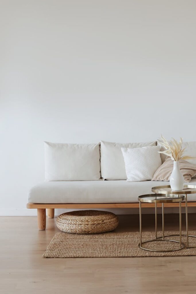 A chic minimalist living room featuring a white sofa with cushions, dried flowers in a vase, and a wooden floor.